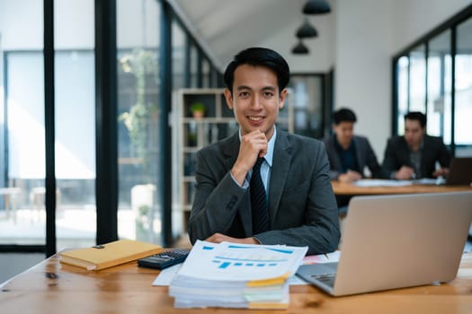 Portrait of an Asian male business owner standing with a computer showing happiness after a successful investment.