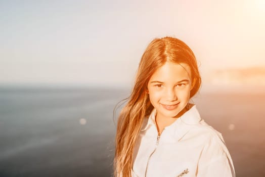 Brown-haired young romantic teenager girl corrects long hair on beach at summer evening wind