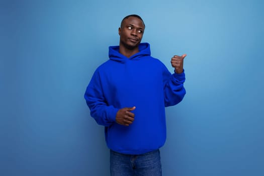 a young african guy in a stylish hoodie demonstrates with his hand on an advertisement on a studio background with copy space.