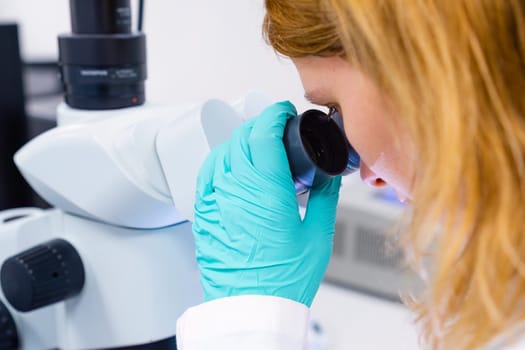 Woman scientist looking through a microscope in a laboratory doing biological analysis.
