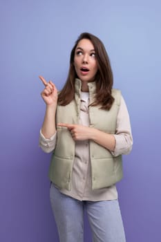 brunette young woman in a vest offers to look to the side pointing a finger.