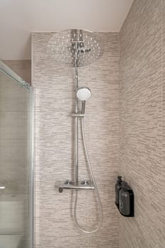 Close-up of a shower cabin with modern fixtures and glass doors and beige tiles in a cozy stylish compact bathroom. Concept shower room for young family.