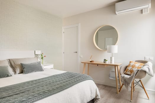 Spacious comfortable bedroom with a double bed, a cosmetic table and a mirror in an eco-boho style interior. The concept of interior renovation in an old apartment.