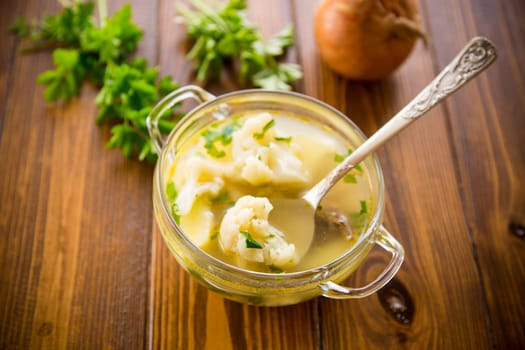 cooked chicken soup with cauliflower and vegetables in a bowl on a wooden table