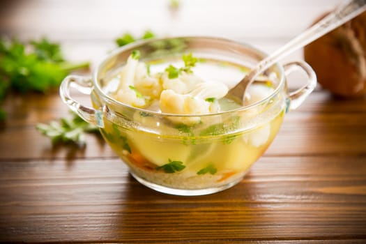 cooked chicken soup with cauliflower and vegetables in a bowl on a wooden table