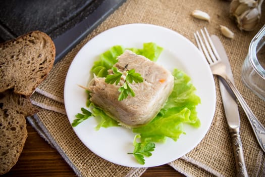 Boiled chicken meat aspic in meat gelatin broth in a plate on a wooden table