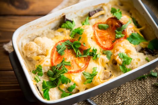 cauliflower baked with chicken fillet and mushrooms under cheese in a ceramic form, on a wooden table.
