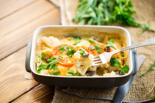 cauliflower baked with chicken fillet and mushrooms under cheese in a ceramic form, on a wooden table.
