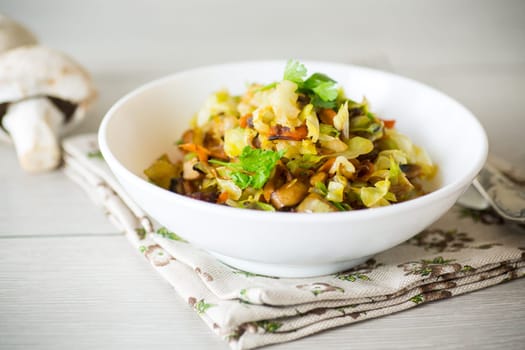 cabbage early fried with mushrooms, carrots and vegetables in a white bowl on a wooden table