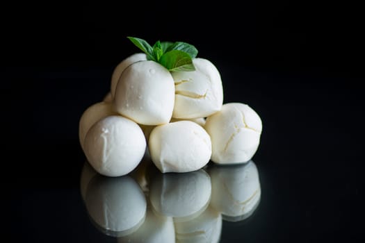 Small balls of traditional mozzarella in a ceramic bowl with mint on a black background