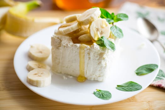 Portion of homemade milk curd with banana slices and honey, with mint in a plate.