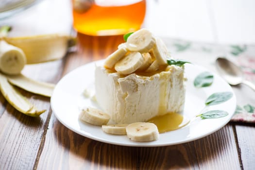 Portion of homemade milk curd with banana slices and honey, with mint in a plate.