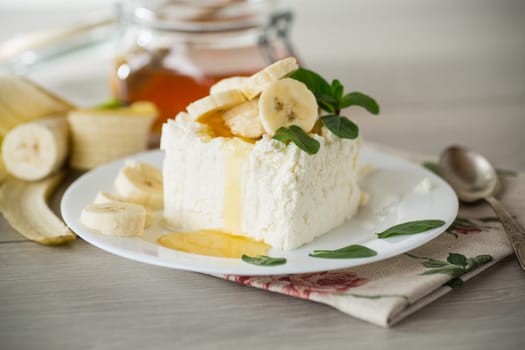 Portion of homemade milk curd with banana slices and honey, with mint in a plate.
