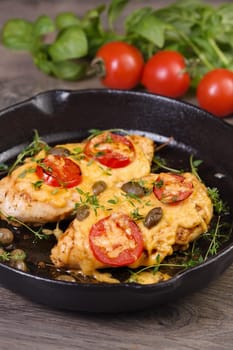 Tender chicken breast baked with tomatoes, capers, herbs under cheese crust in a frying pan