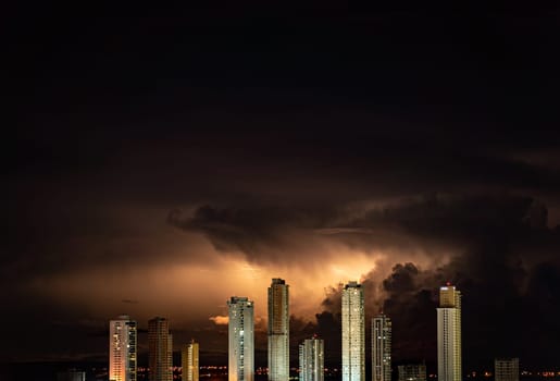 Spectacular high-rise buildings in the cityscape are illuminated by lightning strikes during a dark and stormy night. Plenty of negative space for text.