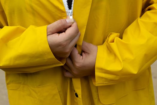 Yellow raincoat with white zipper. The woman zips up her jacket. Clothes for bad weather.
