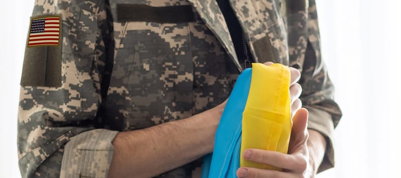 American Flag on Soldiers arm and flag of the Ukraine at background. US military support Ukraine.