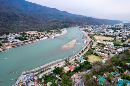 aerial drone shot over ram setu jhula suspension bridge with temples on the bank of river ganga in the holy spiritual city of Rishikesh Haridwar uttarakhand india