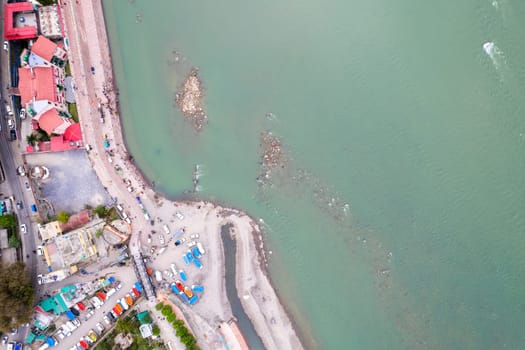 aerial drone shot showing rafts for water adventure sports on the blue waters of ganga river in rishikesh with people watching from the ghats on the riverbank in India