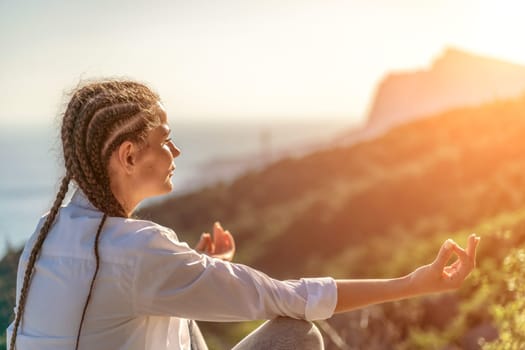 Yoga woman mountains. Profile of a woman doing yoga in the top of a cliff in the mountain. Woman meditates in yoga asana Padmasana.