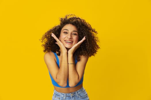 Woman with curly afro hair in a blue t-shirt on. yellow background signs with her hands, look into the camera, smile with teeth and happiness, copy space. High quality photo