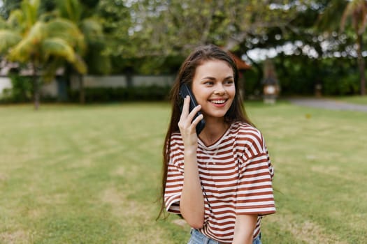 woman happy palm adult tree person blogger t-shirt grass park outside nature beautiful lifestyle smiling phone using talk sitting caucasian shirt summer