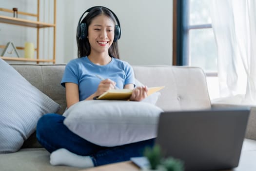 Young Asian woman listening music from headphones and writing note book for her work idea in diary. relax concepts