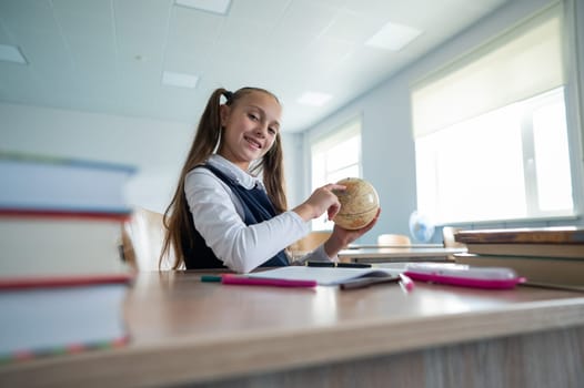 Caucasian schoolgirl sits at her desk at school and studies the globe