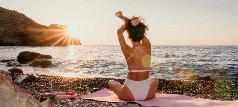 Young woman in swimsuit with long hair practicing stretching outdoors on yoga mat by the sea on a sunny day. Women's yoga fitness pilates routine. Healthy lifestyle, harmony and meditation concept.