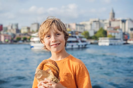 Boy in Istanbul having breakfast with Simit and a glass of Turkish tea. Glass of Turkish tea and bagel Simit against golden horn bay and the Galata Tower in Istanbul, Turkey. Turkiye. Traveling with kids concept.