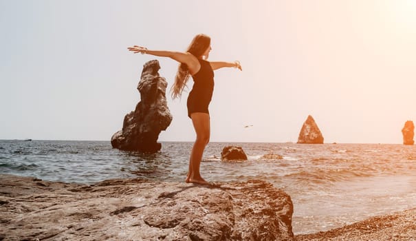 Woman travel sea. Young Happy woman in a long red dress posing on a beach near the sea on background of volcanic rocks, like in Iceland, sharing travel adventure journey