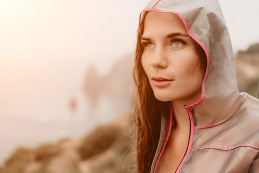 Woman rain park. Happy woman portrait wearing a raincoat with transparent umbrella outdoors on rainy day in park near sea. Girl on the nature on rainy overcast day