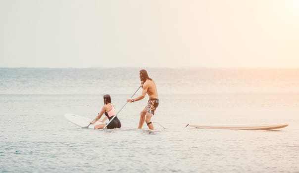 Sea woman and man on sup. Silhouette of happy young woman and man, surfing on SUP board, confident paddling through water surface. Idyllic sunset. Active lifestyle at sea or river