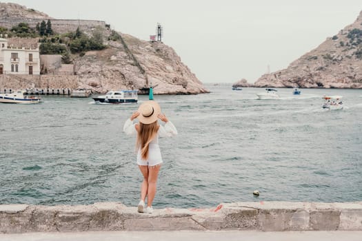 Woman travel sea. Young Happy woman in a long red dress posing on a beach near the sea on background of volcanic rocks, like in Iceland, sharing travel adventure journey