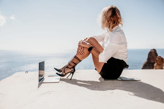 Happy girl doing yoga with laptop working at the beach. beautiful and calm business woman sitting with a laptop in a summer cafe in the lotus position meditating and relaxing. freelance girl remote work beach paradise