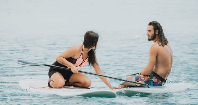 Sea woman and man on sup. Silhouette of happy young woman and man, surfing on SUP board, confident paddling through water surface. Idyllic sunset. Active lifestyle at sea or river