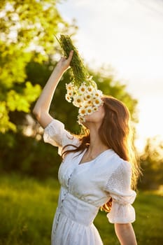 vertical portrait of a red-haired woman in nature during sunset sniffing a bouquet of daisies. High quality photo