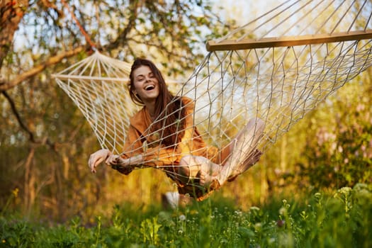 a joyful woman with long hair is lying in a hammock in an orange dress and happily smiling at the camera. A photo taken on the street on the theme of recreation in the country. High quality photo