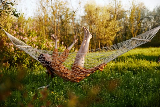 a funny woman is resting in nature lying in a mesh hammock in a long orange dress lifting up her arms and legs. High quality photo