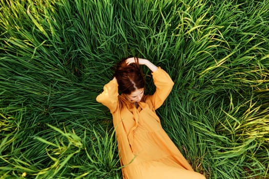 a close horizontal photo of a pleasant woman in a long orange dress resting lying in the tall grass straightening her hair. Street photography, the theme of privacy with nature. High quality photo