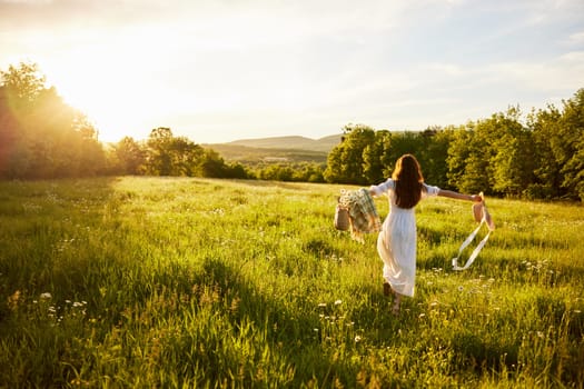 a woman in a light dress with a hat in her hands runs far into the field during sunset. High quality photo