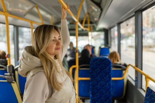 Beautiful young adult caucasian woman stands in the bus and looks into the distance.
