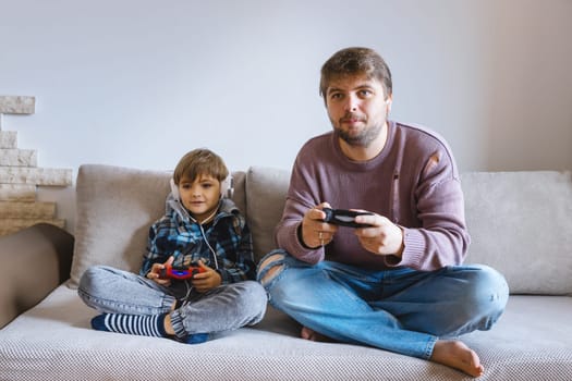 Father And Son Sitting On Sofa In Lounge Playing Video Game.