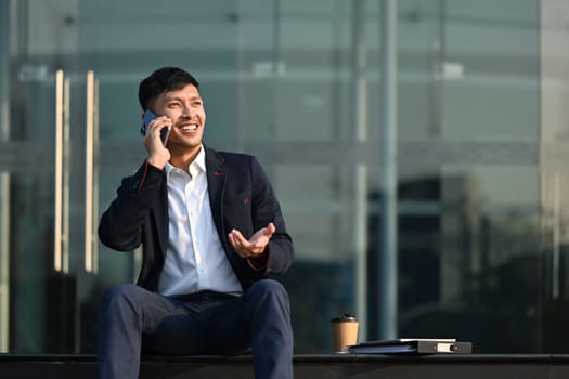 Handsome asian male financial advisor consulting client distantly by mobile phone call, sitting in front of business center.