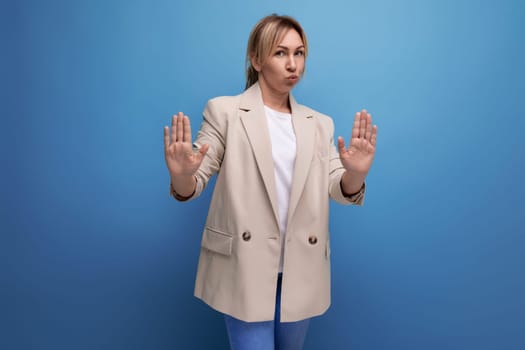 close-up of a doubtful blonde business woman in a jacket on a blue background with copy space.