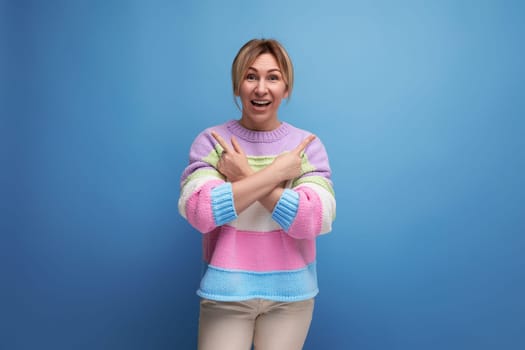 surprised blond woman in a casual look demonstrates about the copy space on the wall on a blue background.