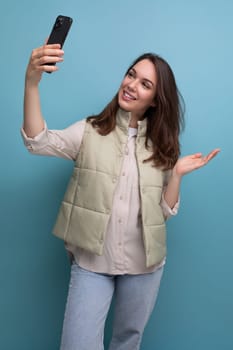 brunette young woman taking selfie using mobile phone on studio background.