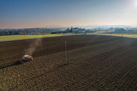 farmer driving a crawler tractor drags a cloud of dust behind, ploughing, power harrowing surface crust breaking to facilitate the birth and seeding of plants on dry soil