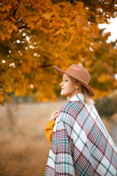 autumn woman in a brown hat, plaid, against the background of an autumn tree.
