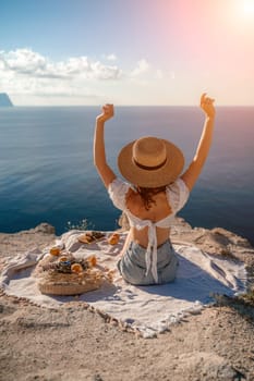 woman sea travel. photo of a beautiful woman with long blond hair in a pink shirt and denim shorts and a hat having a picnic on a hill overlooking the sea.